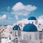 White buildings with blue doomed roofs and a deep blue sky with fluffy white clouds